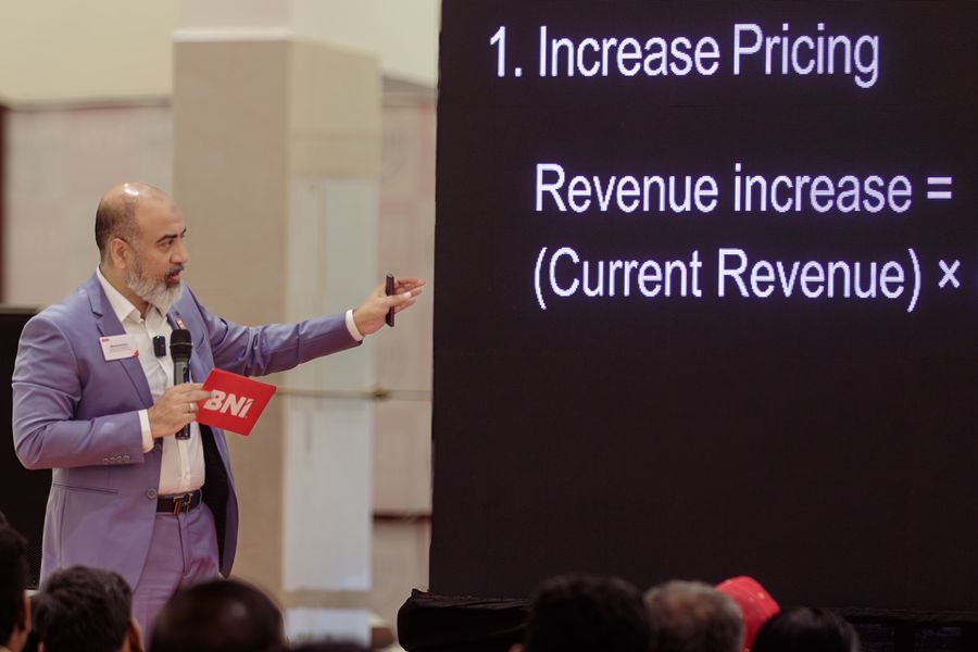 A speaker on stage pointing to a slide about increasing revenue