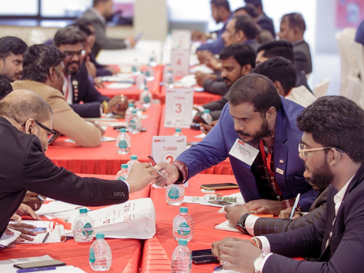Two BNI members reach across Table 2 to exchange a card at the last GrowthCON, with tables 3 and 4 full behind them